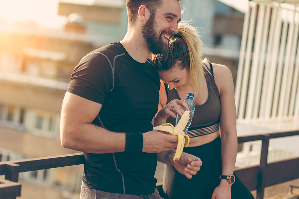 a couple working out. One eating a banana and the other drinking water