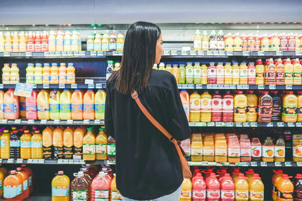 A woman standing in front of shelves filled with juice.