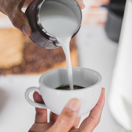 A person pouring liquid into a cup of coffee.